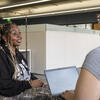 Career Coach and Student talking in a modern office, one sitting with a laptop.